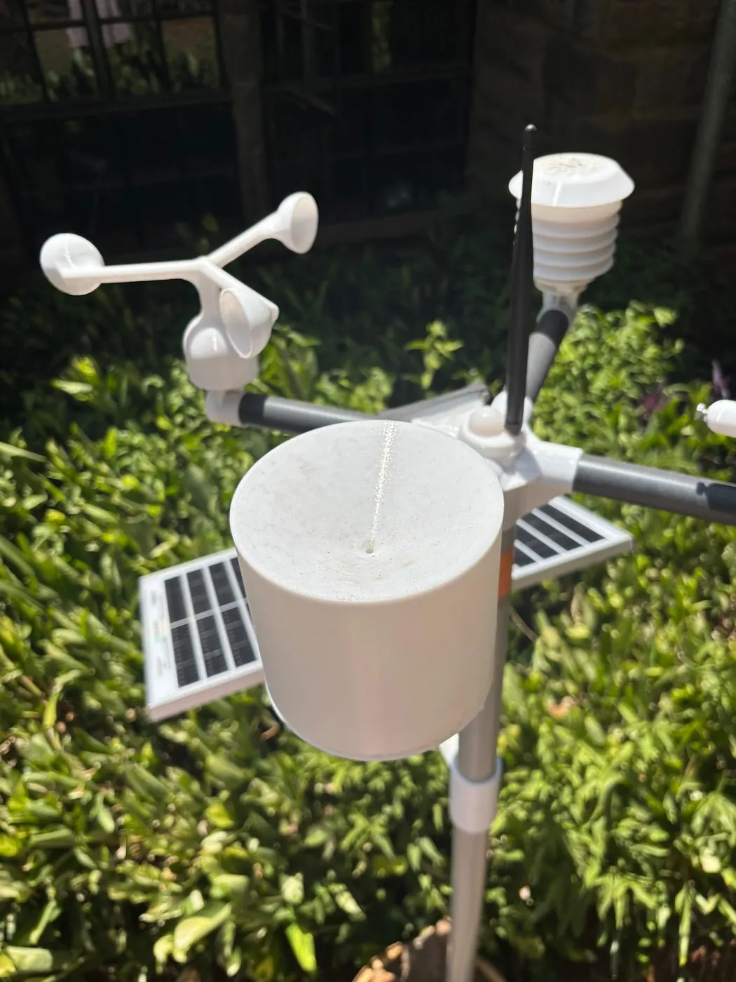 Close view of a weather station rain gauge above green shrubs